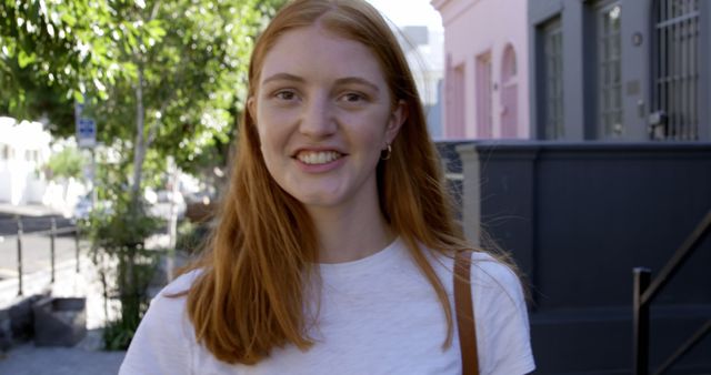 Portrait of happy caucasian woman with red hair standing in sunny city street smiling. Summer, free time, urban living and lifestyle, unaltered.
