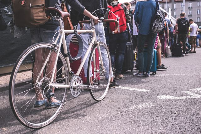 People standing in long queue with luggage and bicycles in city area. This image can be used for illustrating travel, urban transportation, crowd scenarios and public events. Ideal for websites, articles or services related to travel, commuting, public spaces, and city life.