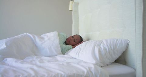 Middle-aged woman sleeping peacefully under white duvet in bright minimalist bedroom