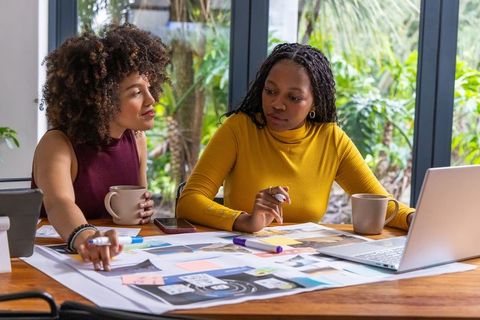 African american women designers collaborating on branding moodboard with laptop in studio