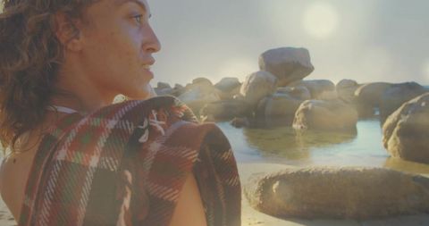 Woman in Plaid Blanket Watching Ocean Rocks on Sunny Shoreline