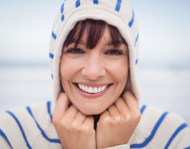 Close up portrait of smiling woman wearing hooded sweater at beach during winter