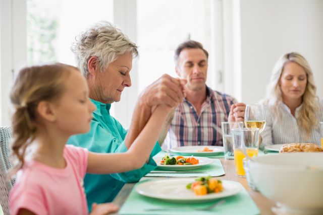 Multi-generation family praying before having meal at home