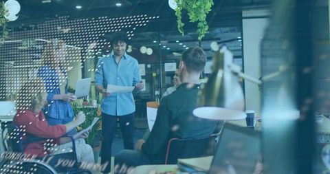 Presenting team leader holding papers in open-plan coworking workspace with diverse colleagues
