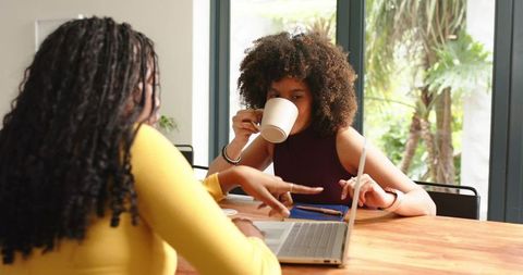 Two colleagues collaborating over laptop while drinking coffee in bright home workspace