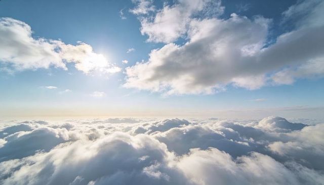 Sunlit cumulus clouds drifting over endless sky with soft stratocumulus glow and warm sun flare