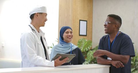 Multicultural medical team collaborating at clinic desk with tablet and smiling faces