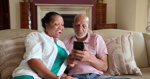 Senior Couple Enjoying Smartphone Together on Cozy Sofa at Home