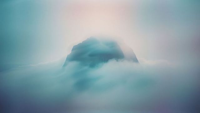 Ethereal Mountain Peak Emerging Above Clouds with Pastel Glow