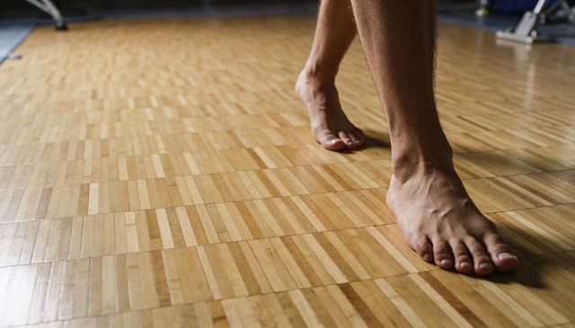 Stepping male bare feet on parquet dance floor closeup showing toes wood grain texture