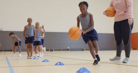 Young Athletes Dribbling Basketballs in Gym under Coach Supervision