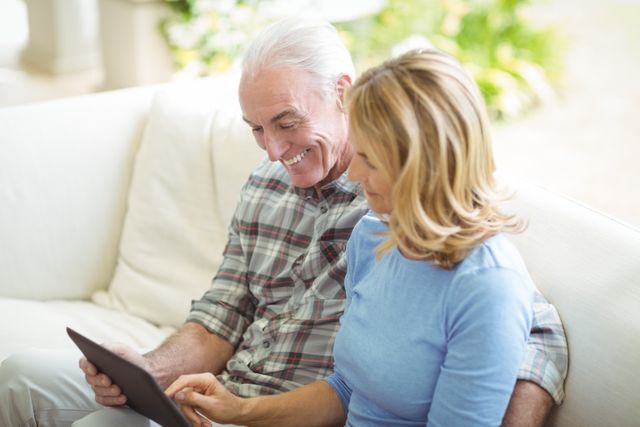 Senior couple using digital tablet in living room at home