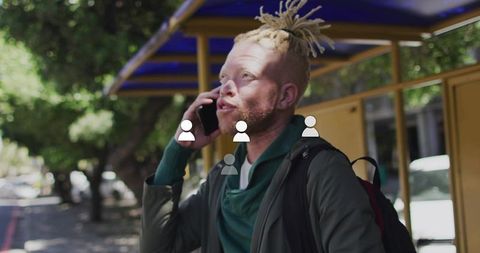 Urban commuter checking phone while waiting at bus shelter under leafy canopy
