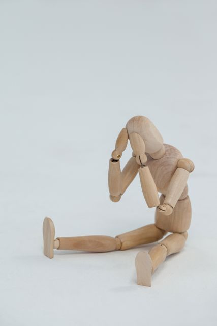 Tensed wooden figurine sitting with hands on head against white background