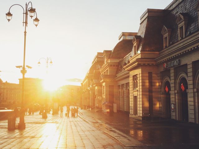 Warm sunset light shining on an urban street lined with historic buildings, creating a picturesque scene. People walking on the street add a sense of daily life. This image is perfect for travel websites, blogs about city exploration, or promoting historic city destinations.