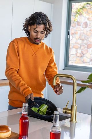Indian man rinsing lettuce in black colander at modern kitchen sink, meal prep