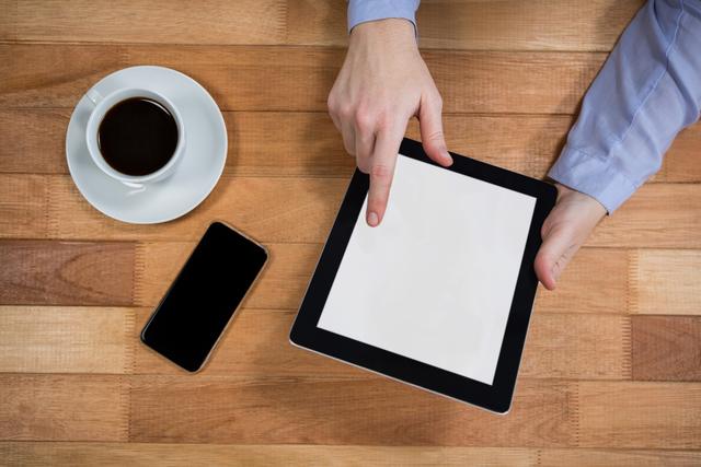 Businesswoman using digital tablet with coffee and smartphone on wooden table. Ideal for illustrating modern work environments, technology use in business, productivity tools, and professional settings.