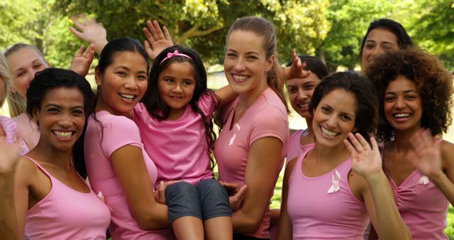 Group of diverse women cheerfully celebrating breast cancer awareness outdoors, dressed in pink shirts and showing their support. Perfect for use in health campaigns, community events, and social awareness promotions.