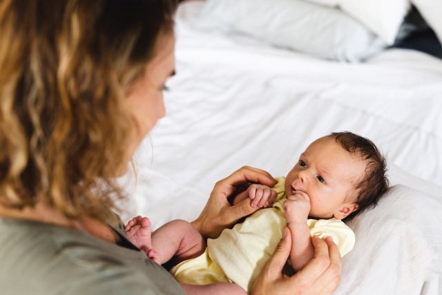 Mid adult caucasian mother lovingly gazing at her cute newborn baby lying on a bed at home. Perfect for use in parenting blogs, family care articles, advertisements for baby products, and motherhood support resources.