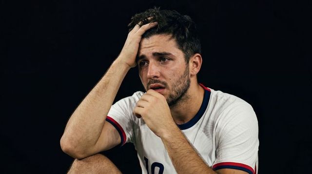 Exhausted number 10 footballer clutching forehead after intense match showing fatigue