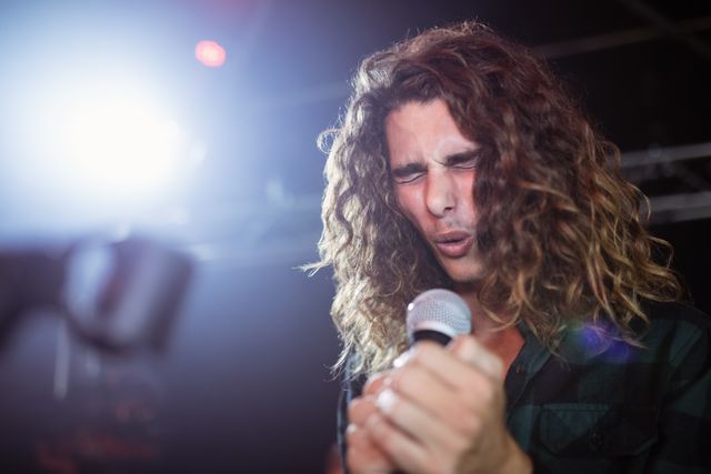 Young male singer passionately performing on stage at a nightclub during a music festival. Ideal for use in articles, blogs, and promotional materials related to live music events, nightlife, entertainment industry, and artist profiles.