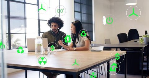 Two coworkers reviewing sustainability metrics on laptop while collaborating at office