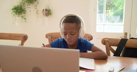 African american boy studying at home with laptop and headphones, focused remote learning