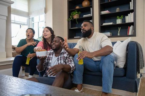 Diverse friends excited watching tv together at home