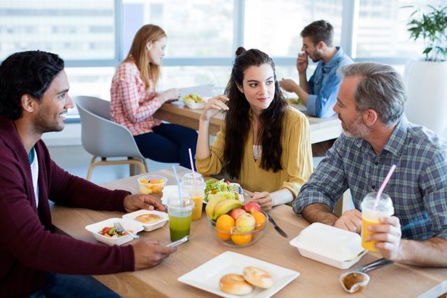 Creative business team discussing ideas during lunch break in a modern office. Ideal for illustrating workplace collaboration, team building, and casual business meetings. Suitable for use in articles about office culture, teamwork, and productivity.
