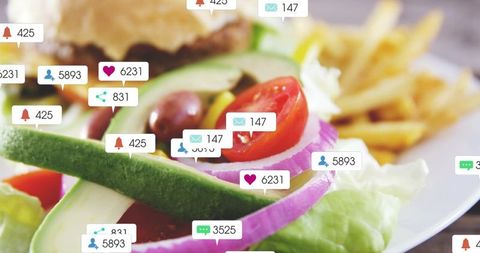 Fresh avocado salad showing cherry tomatoes, red onion and olives with blurred burger
