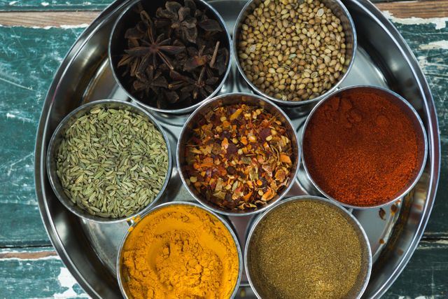 This image shows an overhead view of a traditional spice box containing various spices like turmeric, coriander, chili powder, fennel, star anise, and more. Ideal for use in culinary blogs, recipe websites, cooking tutorials, and food-related articles. Perfect for illustrating the diversity and richness of spices used in traditional cooking.