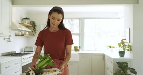 Woman Arranging Vegetables in Eco-Friendly Bag in Bright Kitchen