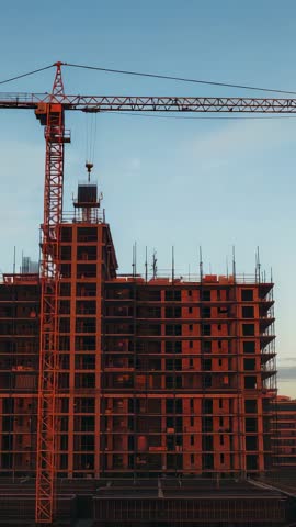 Tower crane lifting precast panels while constructing high-rise concrete frame in urban development