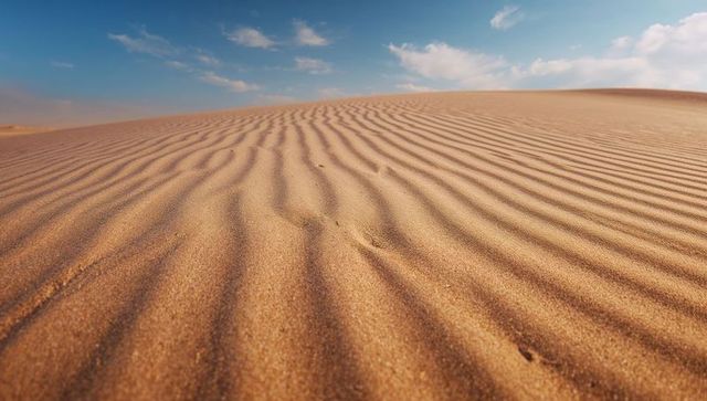 Golden sand ripples leading toward dune crest under blue sky with scattered clouds