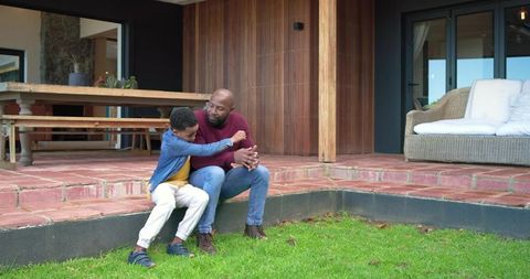 African american father and son sharing quiet moment on home patio steps near wicker sofa