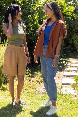 Diverse female friends chatting in sunny backyard garden, casual summer fashion