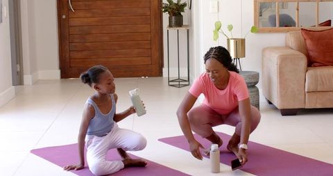 Mother and daughter practicing yoga at home on purple mats drinking water and smiling
