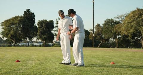 Two cricketers discussing strategy during outdoor cricket training on grassy field
