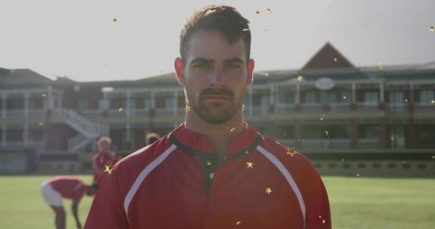 Male athlete standing confidently on backlit sports field while teammates warm up