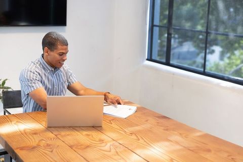 African-american professional reviewing documents at bright office desk with laptop and daylight