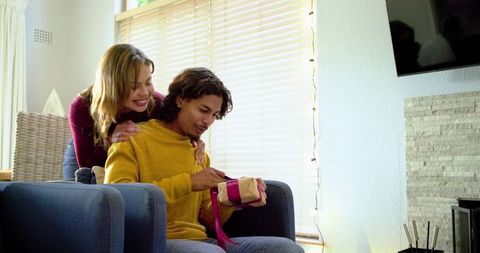 Couple sharing cozy moment while unwrapping magenta-ribboned gift in sunlit living room