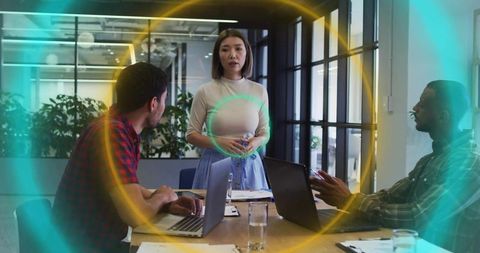 Presenting Asian businesswoman leading team meeting in modern boardroom with laptops