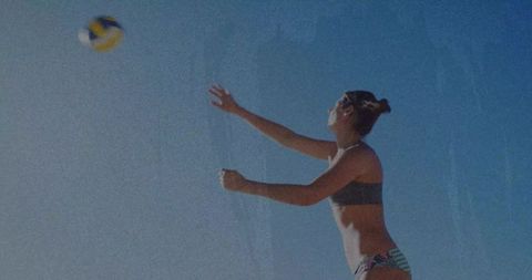 Athletic woman reaching and jumping for beach volleyball under clear blue sky
