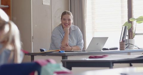 Female teacher smiling at her desk with laptop in classroom