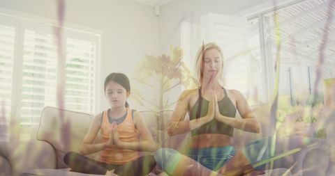 this image depicts a mother and daughter practicing yoga together, symbolizing family bonding and wellness. their serene environment is enhanced by the calming overlay of softly moving grass, merging indoor tranquility with natural elements. ideal for promoting mindfulness, home workouts, or family-oriented wellness content.