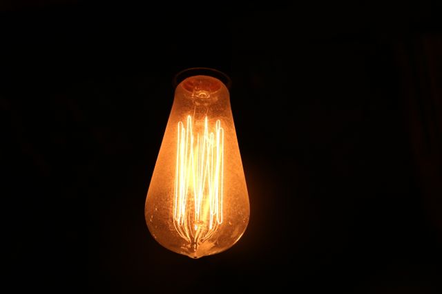 Bright and warm glowing vintage Edison light bulb against dark background. Highlights unique filament design, ideal for showcasing nostalgic, retro-themed, or industrial decor. Perfect for use in advertising, interior design projects, energy concepts, and blogs about home lighting or historical technology.