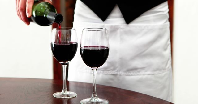 A waiter, middle-aged, is pouring red wine into a glass, with copy space. Capturing the essence of fine dining, the image reflects a moment of service and hospitality.