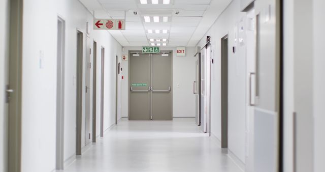 Clean, well-lit hospital corridor with emergency exit signs and closed doors, highlighting the sterile and organized nature of a medical facility. Useful for illustrating concepts related to healthcare infrastructure, emergency protocols, and modern medical environments.