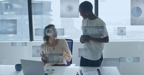 Two women collaborating on data analytics and strategy in modern office with city view
