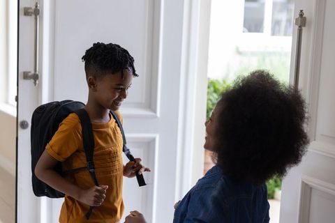 African american mother helping son with backpack at front door smiling morning goodbye